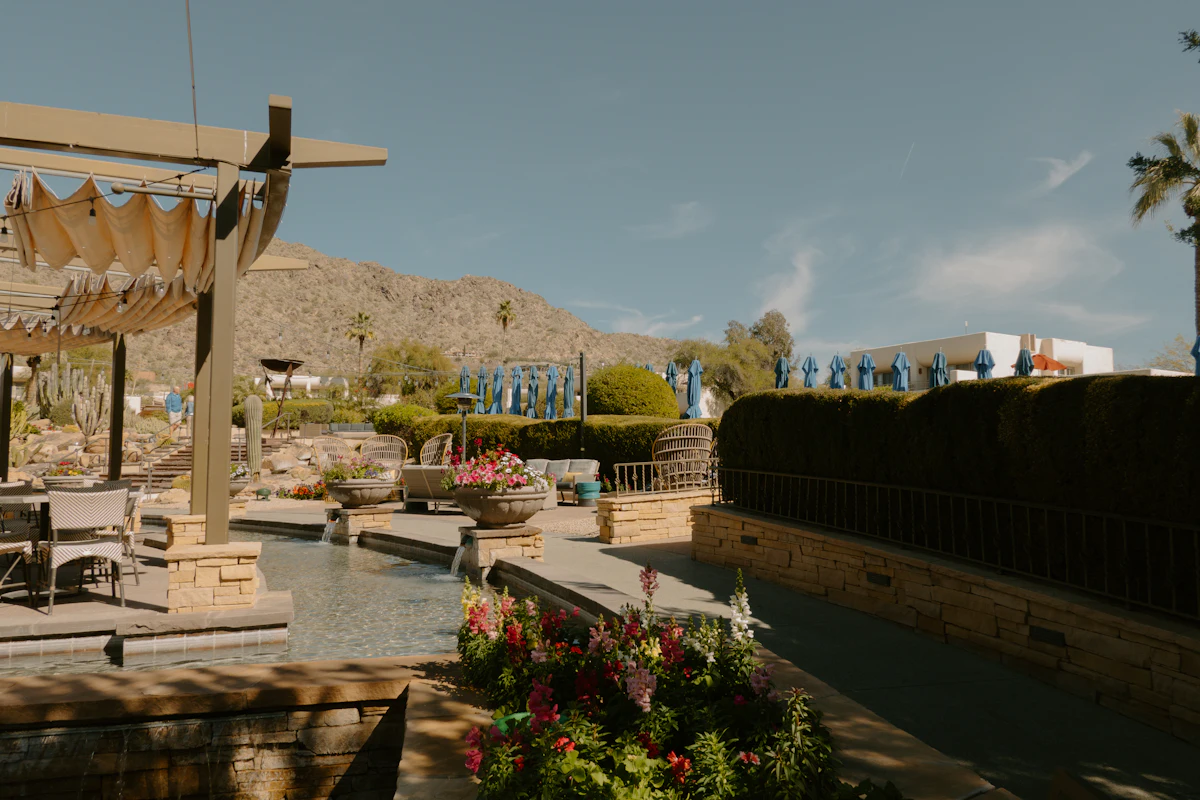A desert backyard patio with a long water feature, flowering beds and mountains beyond